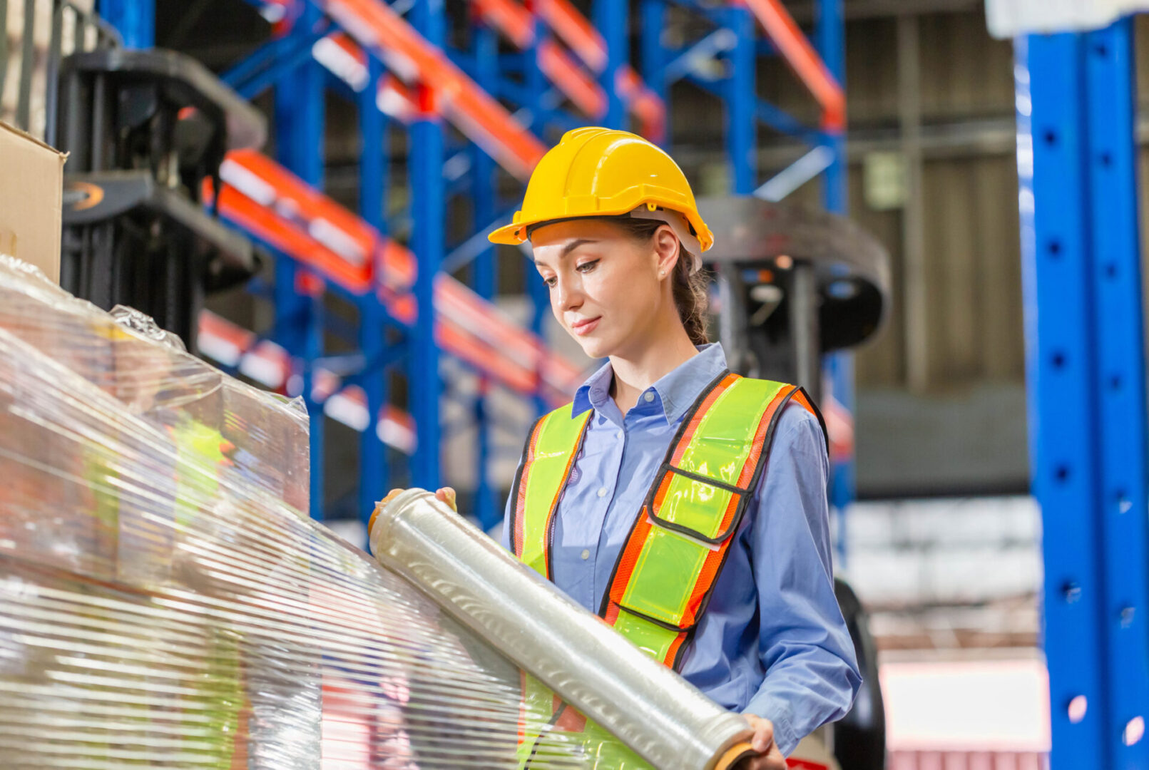 Female worker wrapping boxes in stretch film at warehouse, Worker wrapping stretch film parcel on pallet in factory warehouse